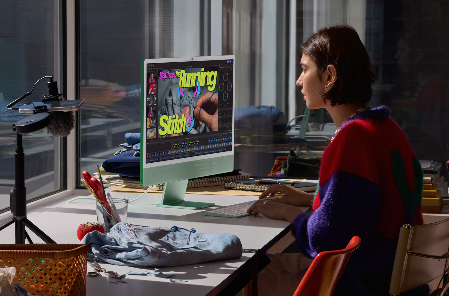 A person working at a desk with a green iMac, typing on a Magic Keyboard and using a Magic Mouse, watching a sewing tutorial